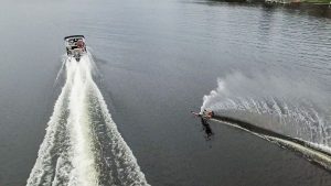 A pontoon is racing down the lake while towing a water-skier.