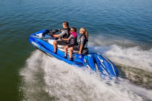 A man, young boy and young girl riding a blue Yamaha jet ski while pulling an inflatable raft behind.