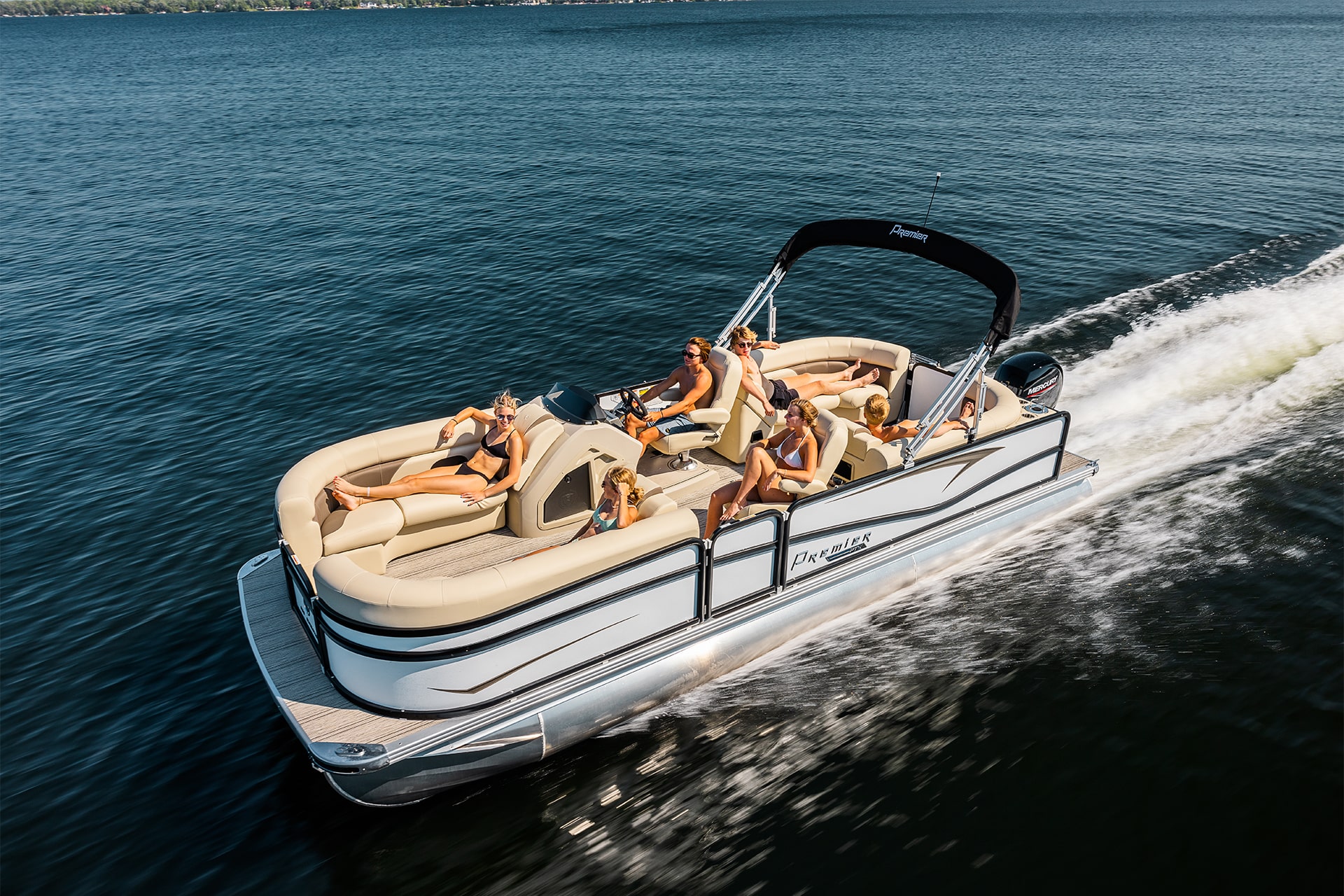 A high up view of a group of young adults racing down the lake in a Premier tritoon. A young man is driving, while every one is sitting in a seat relaxing.