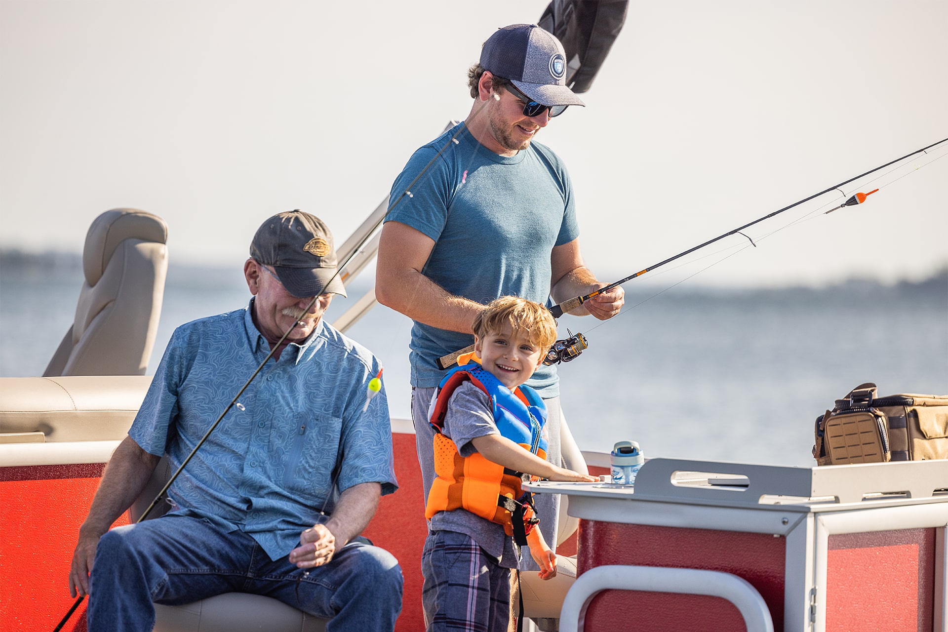 Grandfather, father and son getting their fishing poles ready on a pontoon.