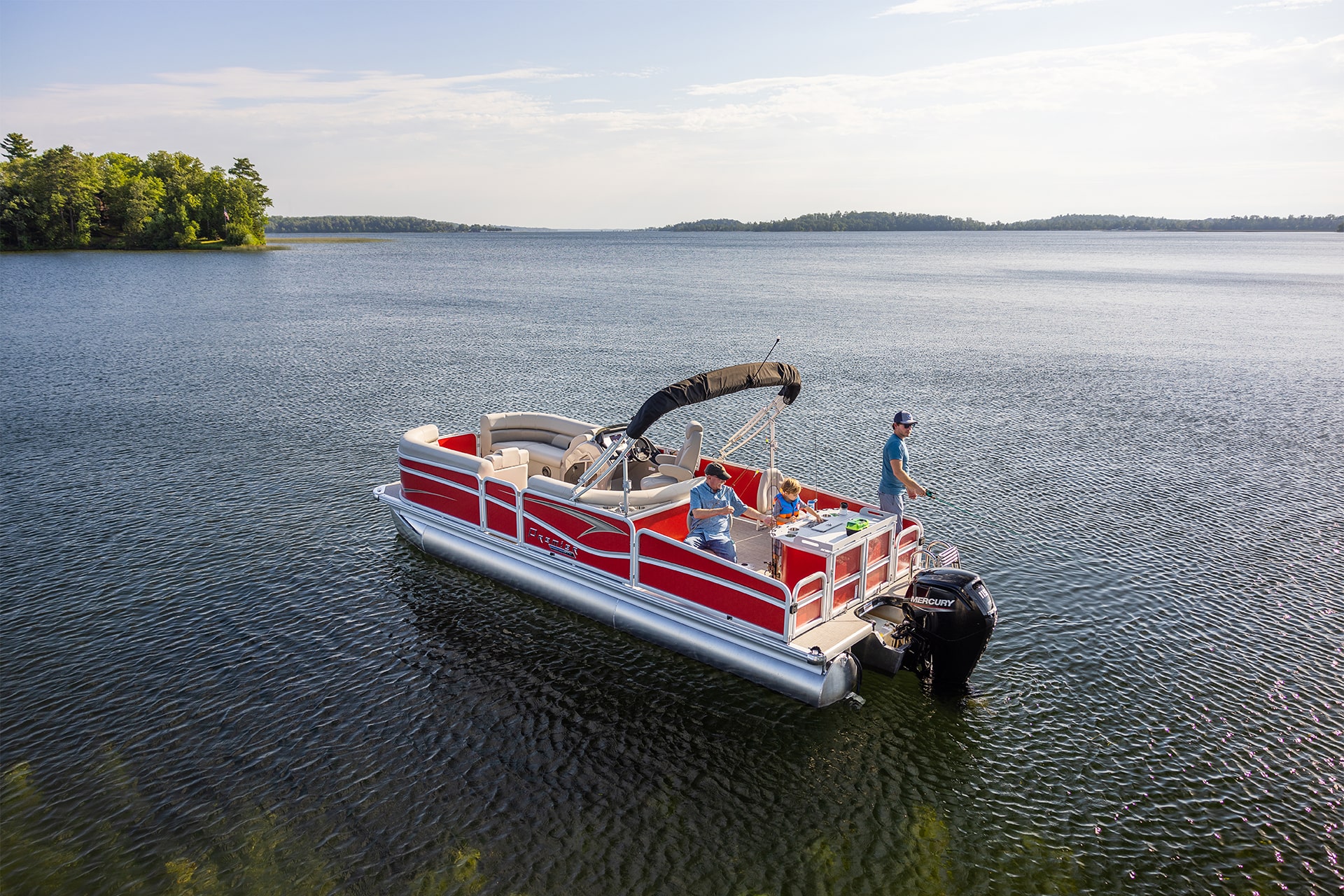 A grandfather, father and son on a Premier pontoon fishing off the back on a lake during a sunny day.