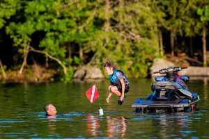 A young boy jumping off a jet ski into the water to meet his swimming dad.